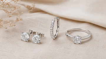 Editorial shot of a pair of round moissanite stud earrings, a slim moissanite hoop, and a single solitaire ring, all in 925 sterling silver with a soft white-gold finish - Sensitive Stones