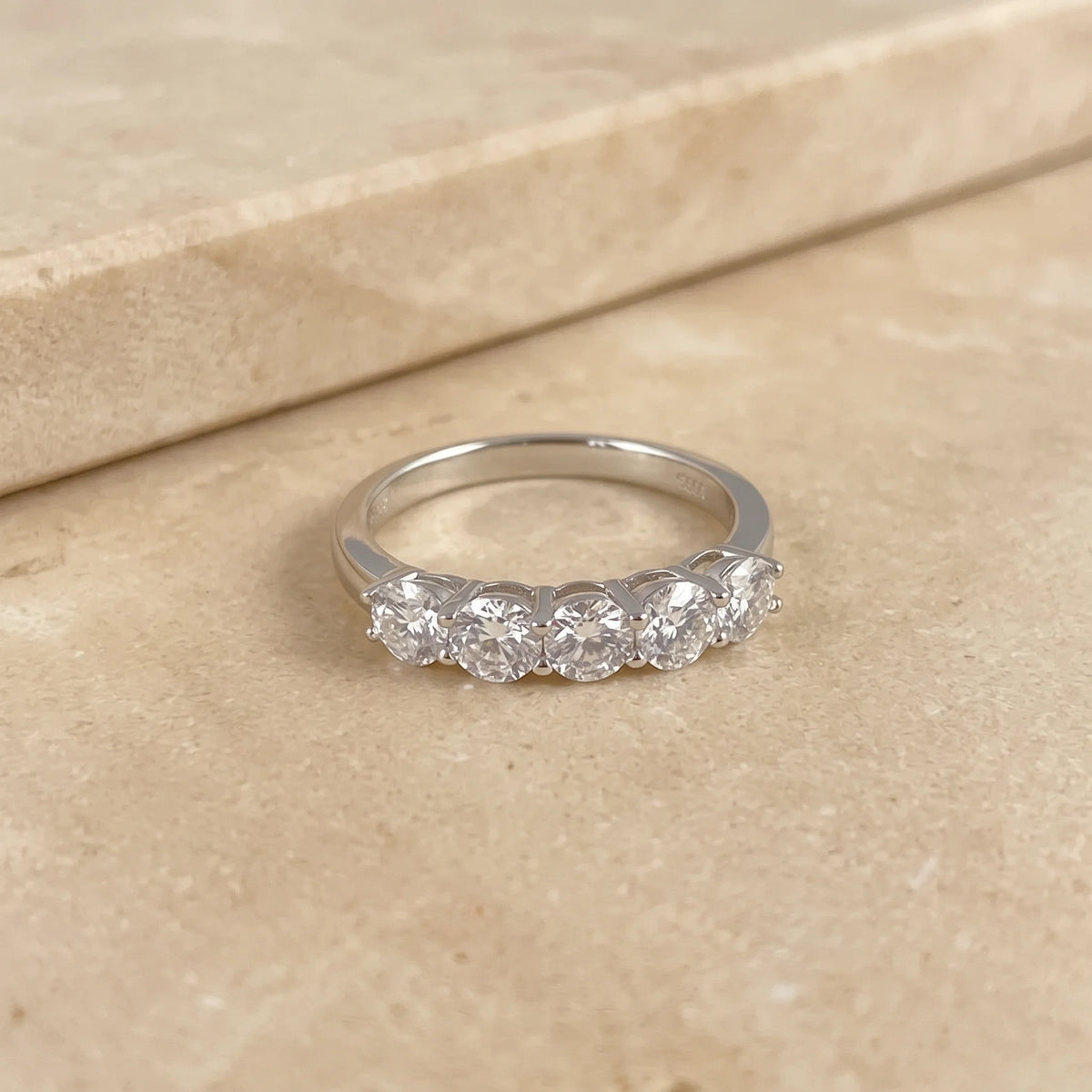 1.5ct five stone moissanite wedding band in 925 sterling silver white gold resting on a cream stone ledge - Sensitive Stones
