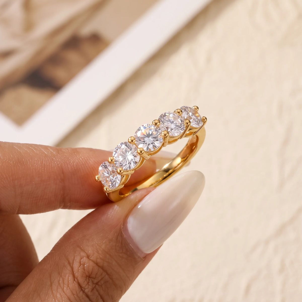 1.5ct five stone moissanite wedding band in yellow gold finish held between fingertips - Sensitive Stones