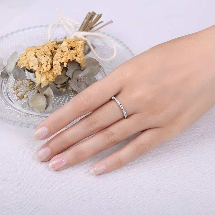 Elegant hand modeling a moissanite eternity ring under natural lighting, showcasing its brilliant sparkle and delicate design.