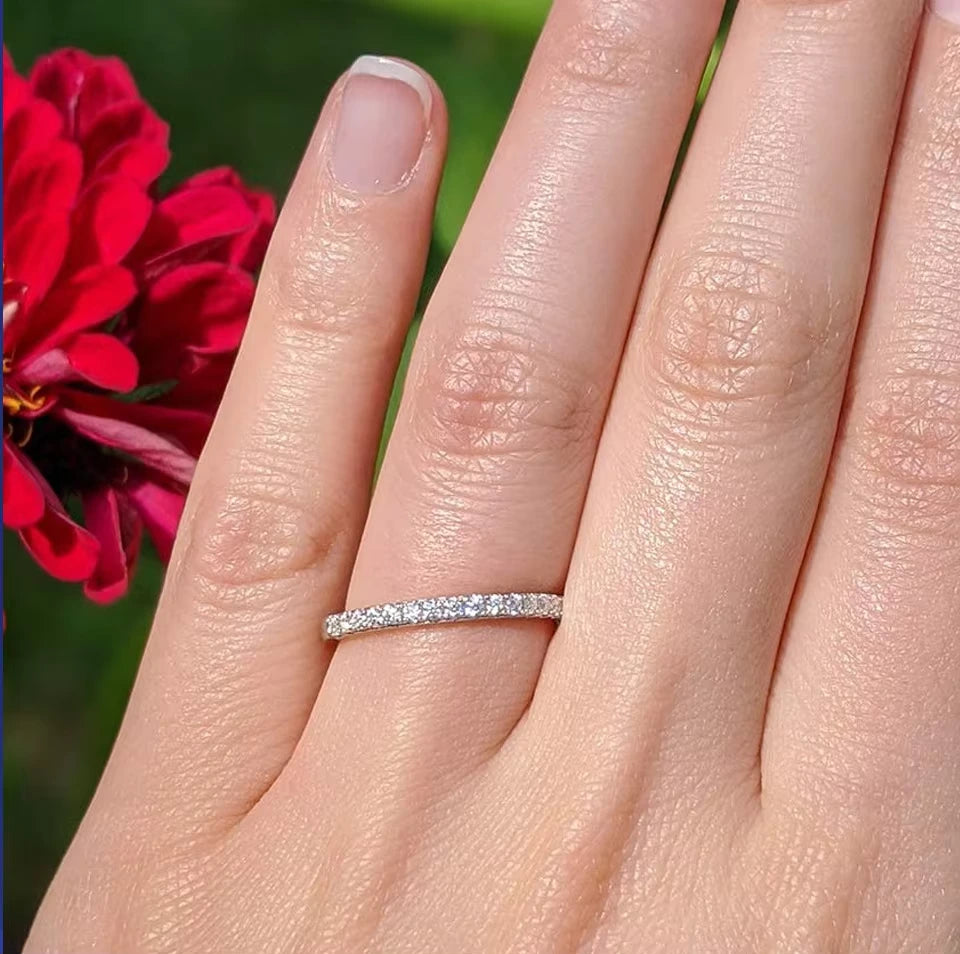 Close-up of hand wearing 1.86 CT Moissanite Eternity Ring next to vibrant red flowers, showcasing the ring’s brilliant sparkle in natural light.