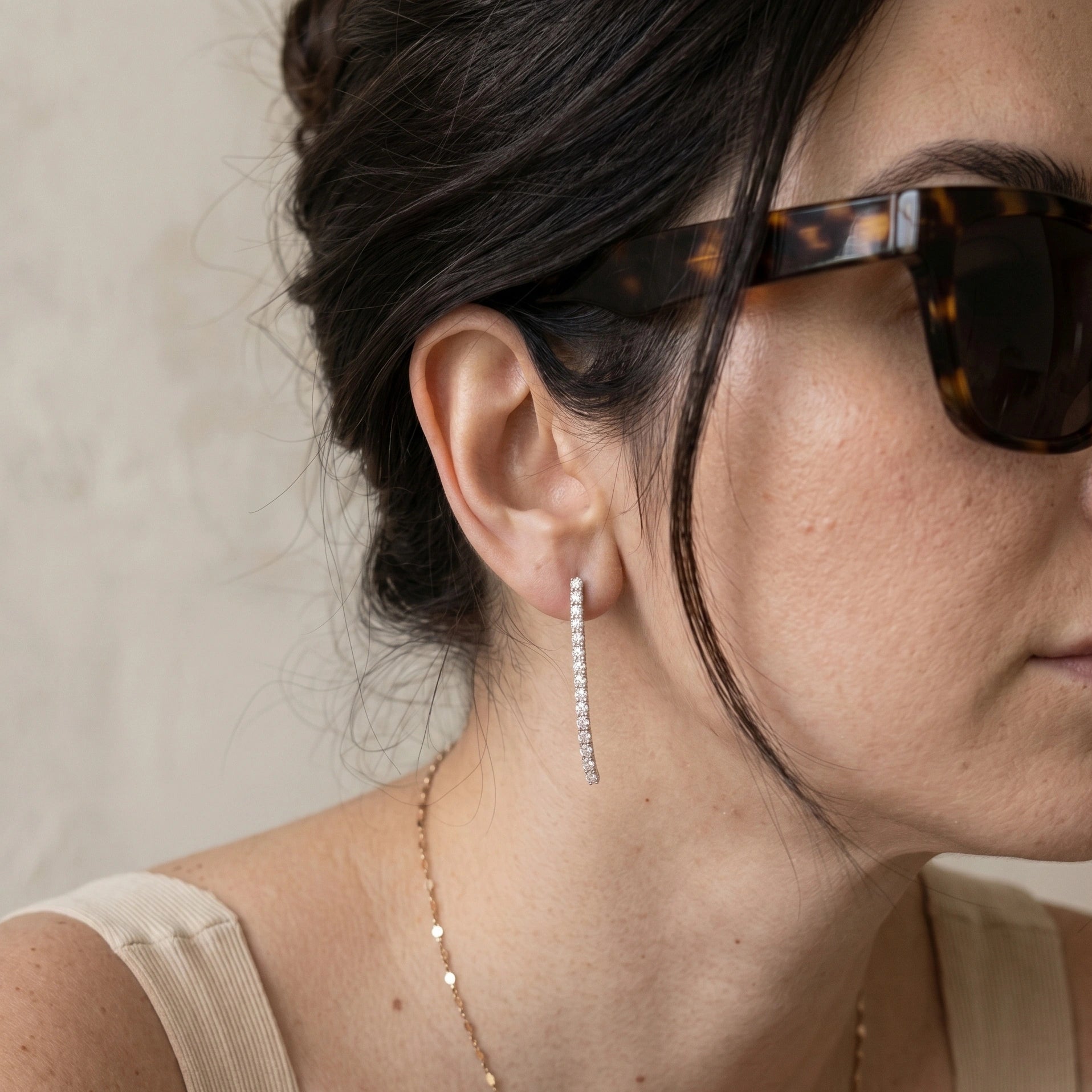 Woman wearing 1.8ct VVS1 moissanite linear drop earrings in 925 sterling silver with 18K gold plating, styled with sunglasses and a neutral top