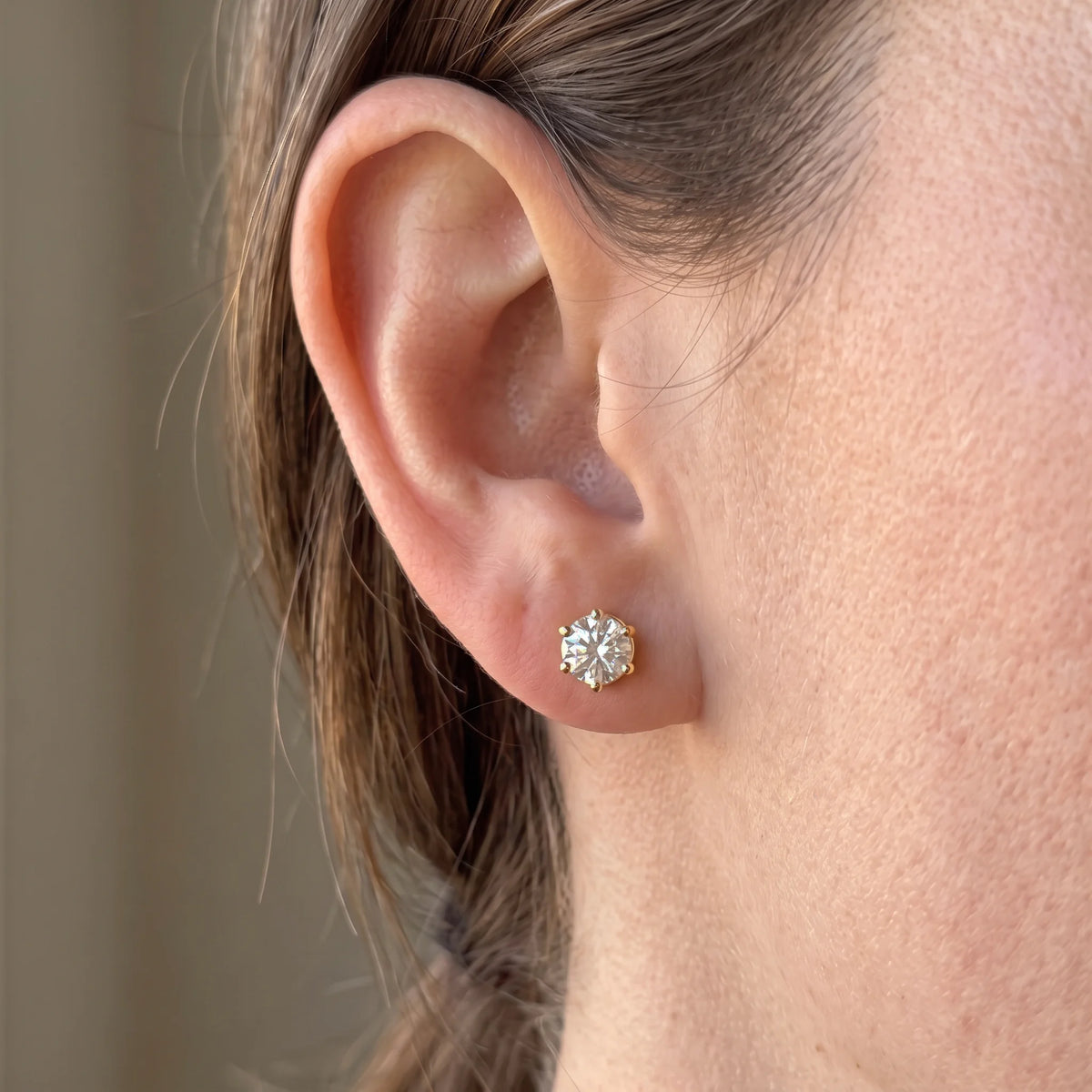 Woman wearing a 6-prong moissanite solitaire stud earring in 14K yellow gold filled showing natural size on the ear - Sensitive Stones