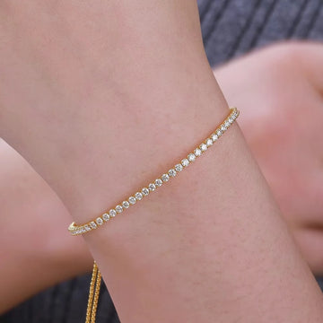 Close-up of 18K yellow gold plated 925 sterling silver 2mm moissanite tennis bracelet worn on wrist, showing full continuous round stone setting with brilliant sparkle against grey outfit - Sensitive Stones