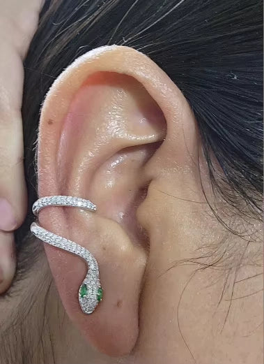 Close-up view of sterling silver moissanite snake ear climber fitting the ear contour with vivid green nano eyes.