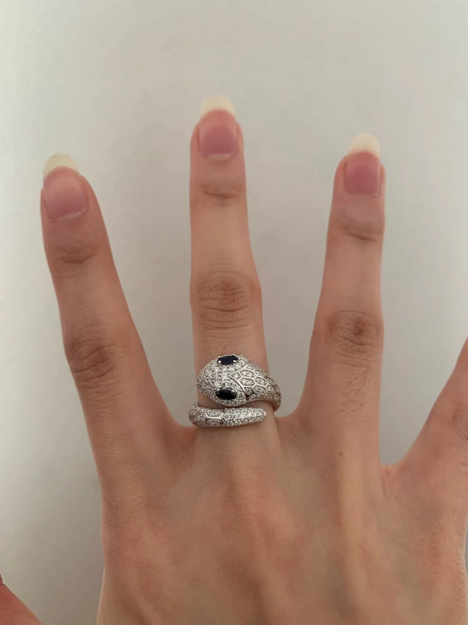 Moissanite snake ring with sapphire blue color eyes, worn on finger. Intricate 925 sterling silver serpent design showcasing detailed texture and sparkle.
