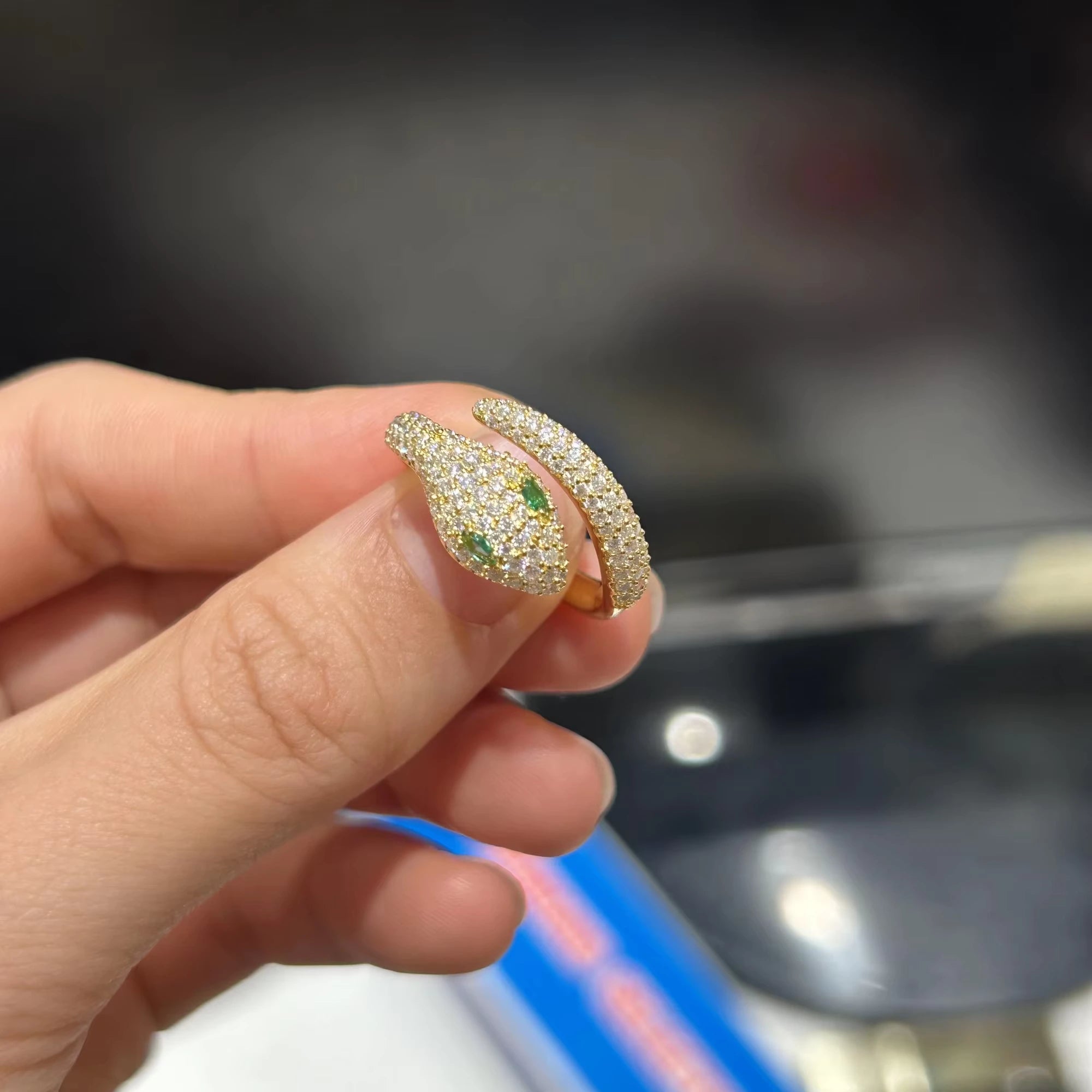 Close-up of moissanite snake ring with emerald green color stones for the eyes, crafted in sterling silver with detailed scales and high-polish 18K yellow gold finish.