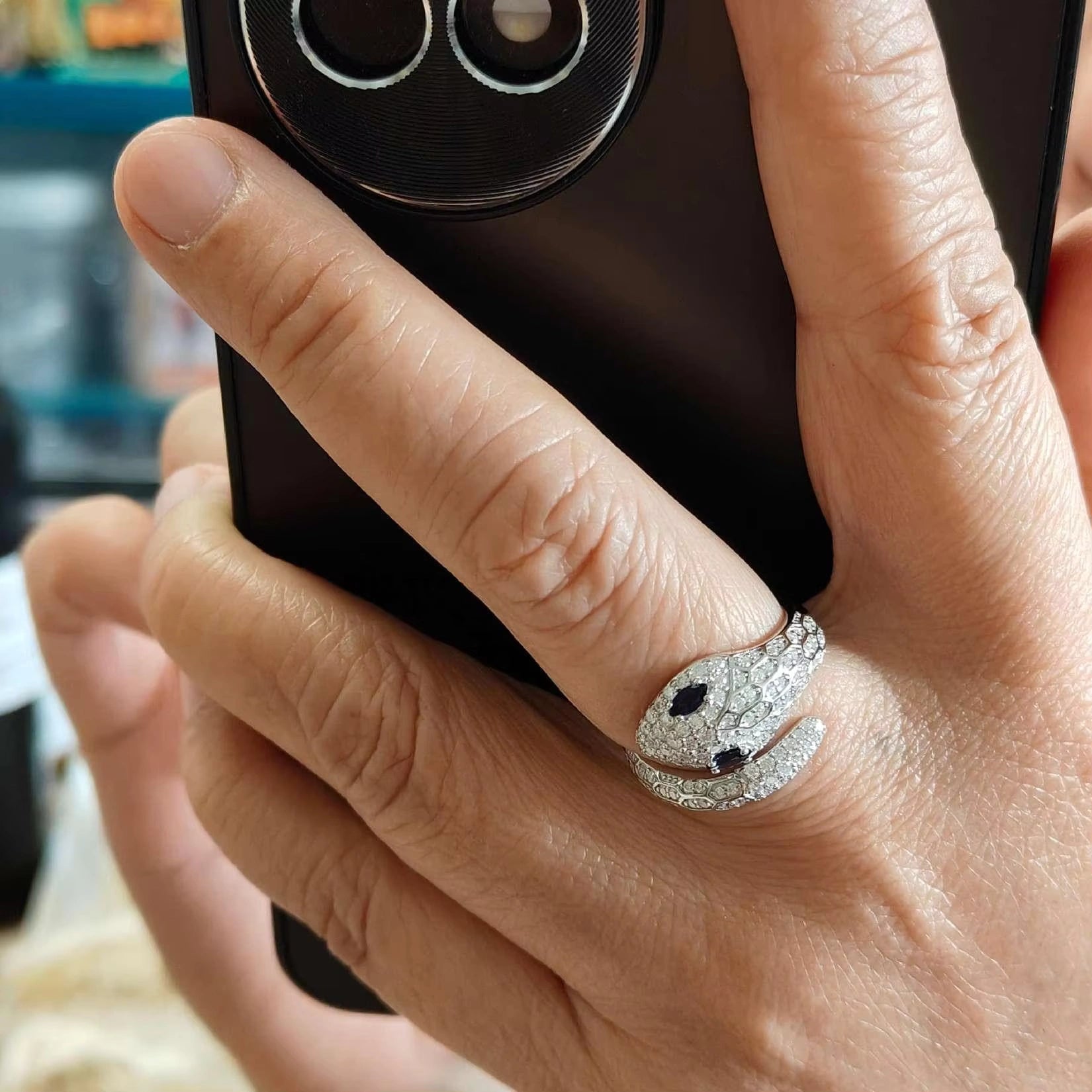 Modern 2025 Moissanite Snake Ring on woman's hand holding a smartphone, showcasing sparkling design.
