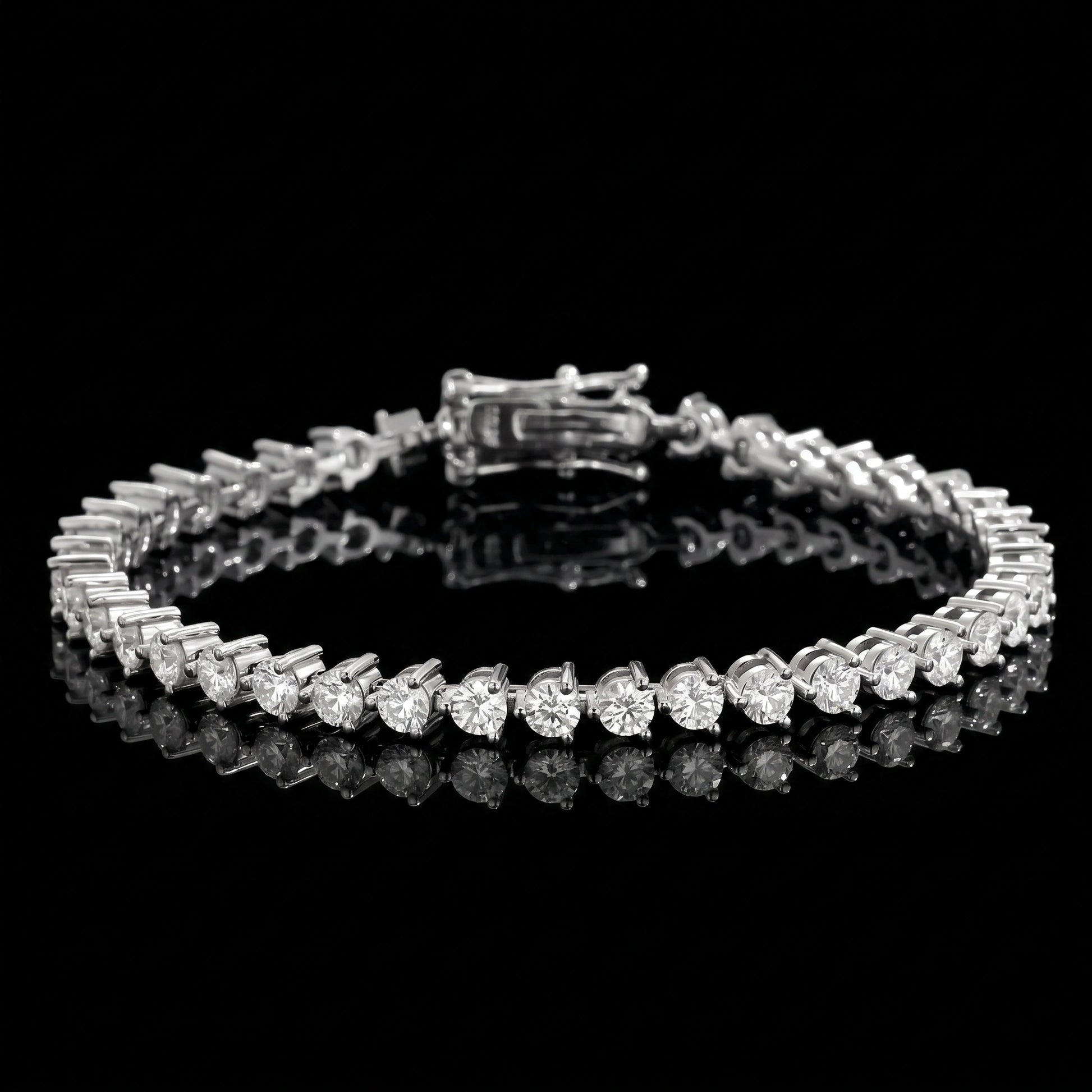 A 3-prong moissanite tennis bracelet with clear round-cut stones set in 925 sterling silver with white gold finish, displayed on a reflective black surface against a black background - Sensitive Stones