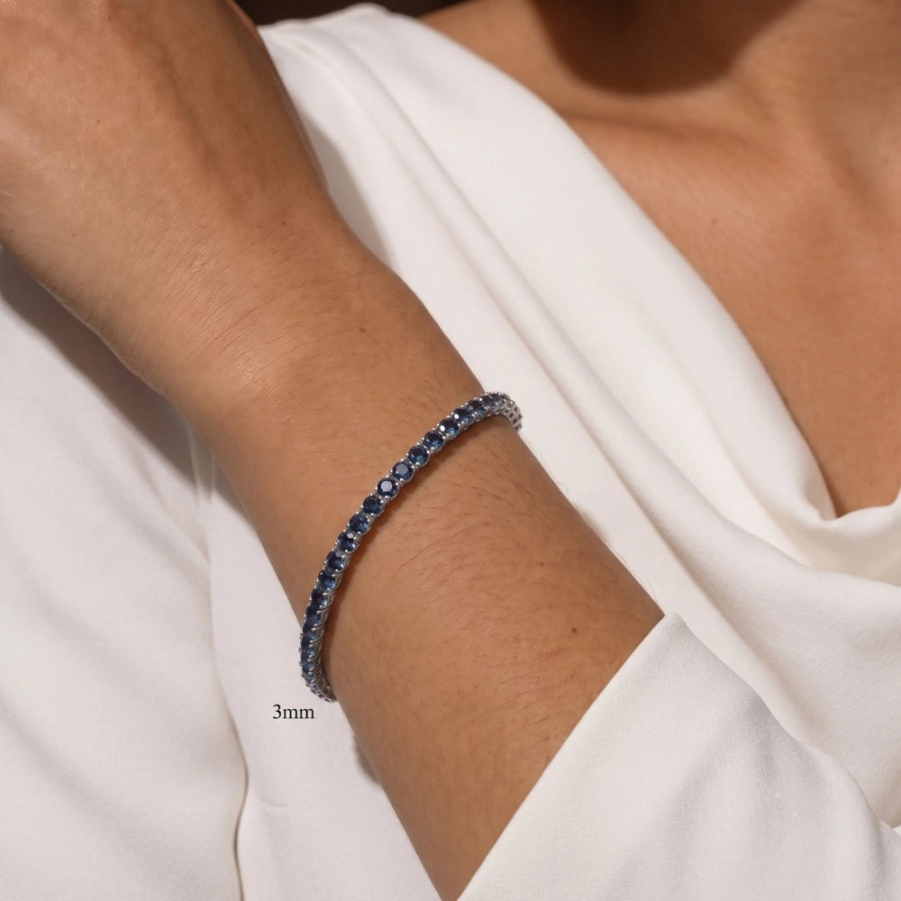 Woman wearing a delicate 3mm full blue moissanite tennis bracelet, color-shifting round-cut stones in 925 sterling silver - Sensitive Stones