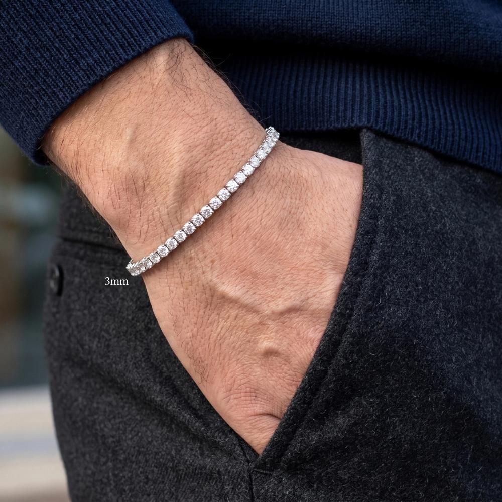 A man's wrist wearing a sparkling white gold 3mm moissanite tennis bracelet, styled with a navy knit sweater and charcoal trousers - Sensitive Stones