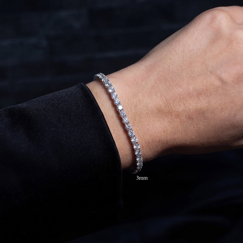 A woman's wrist wearing a white gold 3mm moissanite tennis bracelet with clear stones, against a dark background - Sensitive Stones