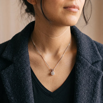 Woman wearing the 4-prong moissanite solitaire necklace in a white gold finish on a box chain with a dark knit sweater - Sensitive Stones