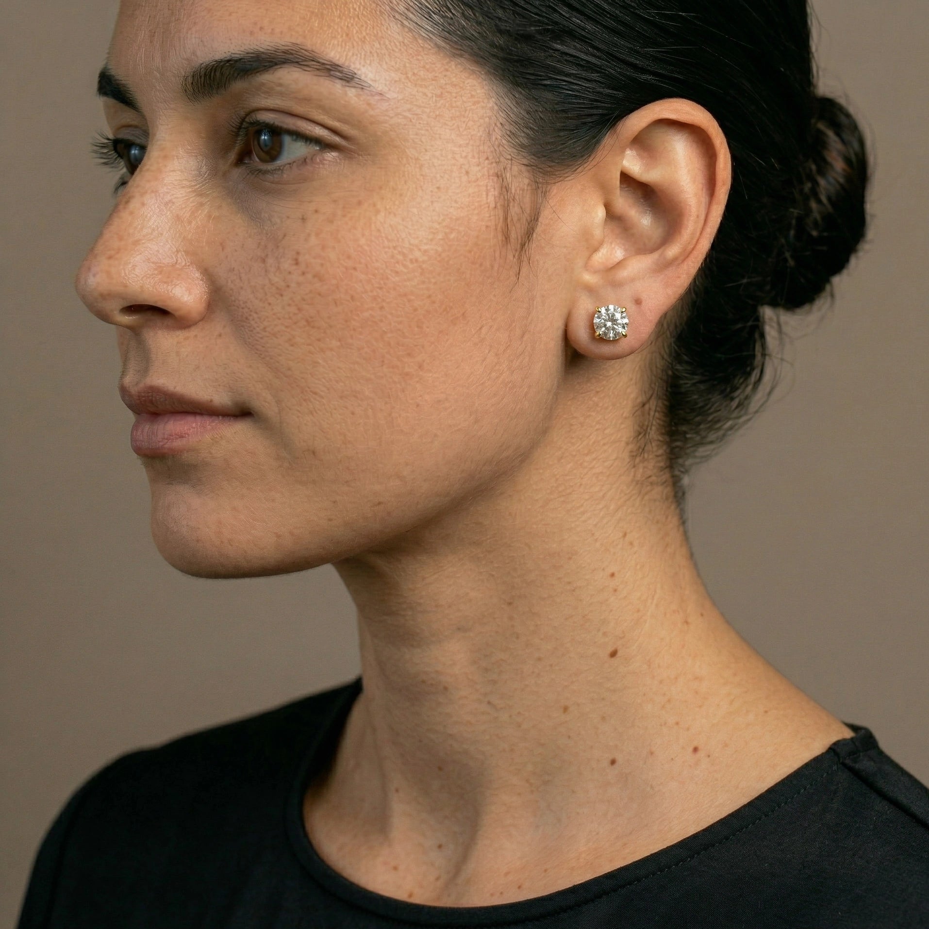 Woman wearing round cut moissanite solitaire stud earring in 4-prong sterling silver with 18k gold finish in black outfit – Sensitive Stones