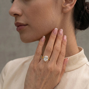Woman wearing a 4-prong oval moissanite engagement ring in 14K gold filled on her ring finger