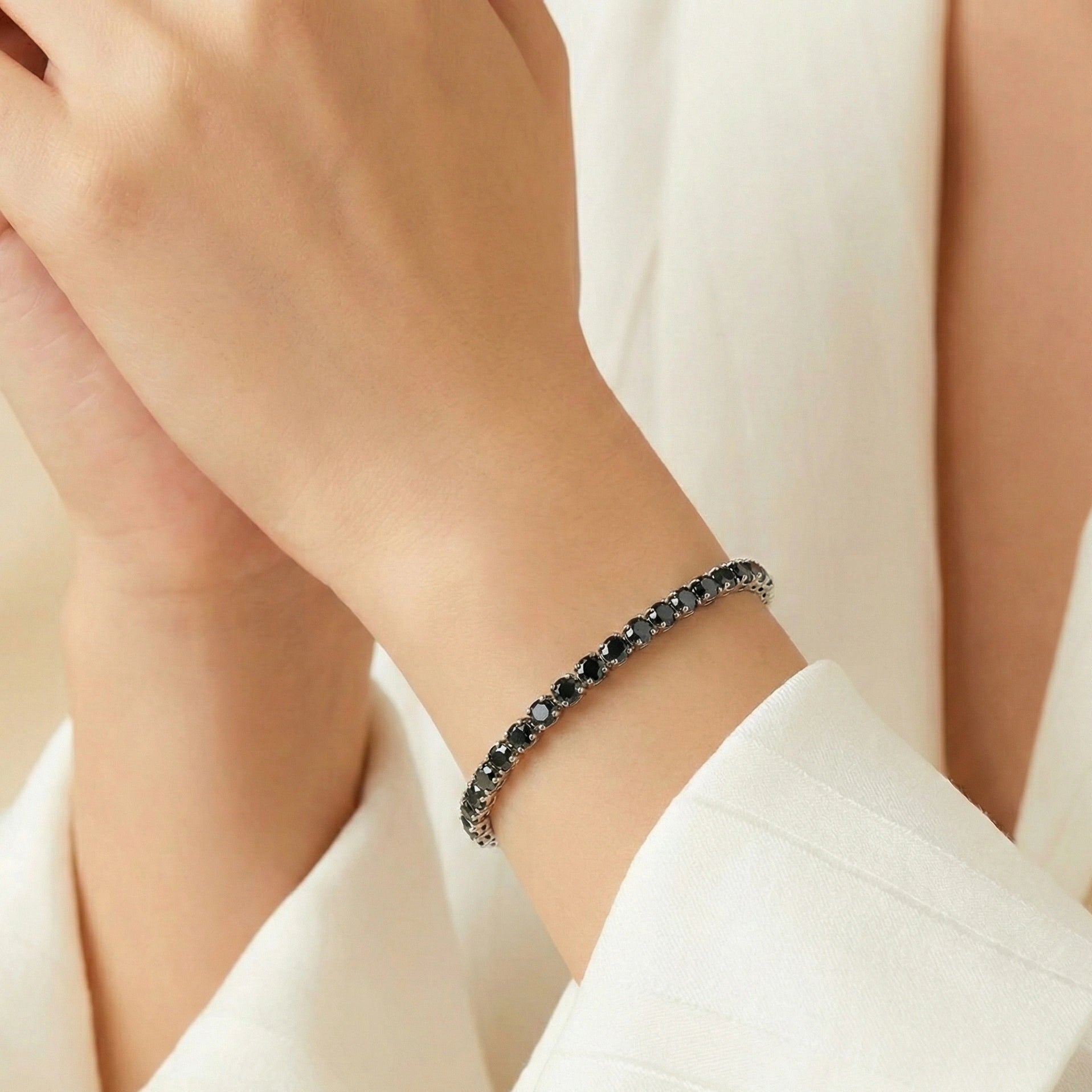 Woman wearing 4 mm black moissanite tennis bracelet in white gold plating, elegant wrist close-up with soft beige background – Sensitive Stones