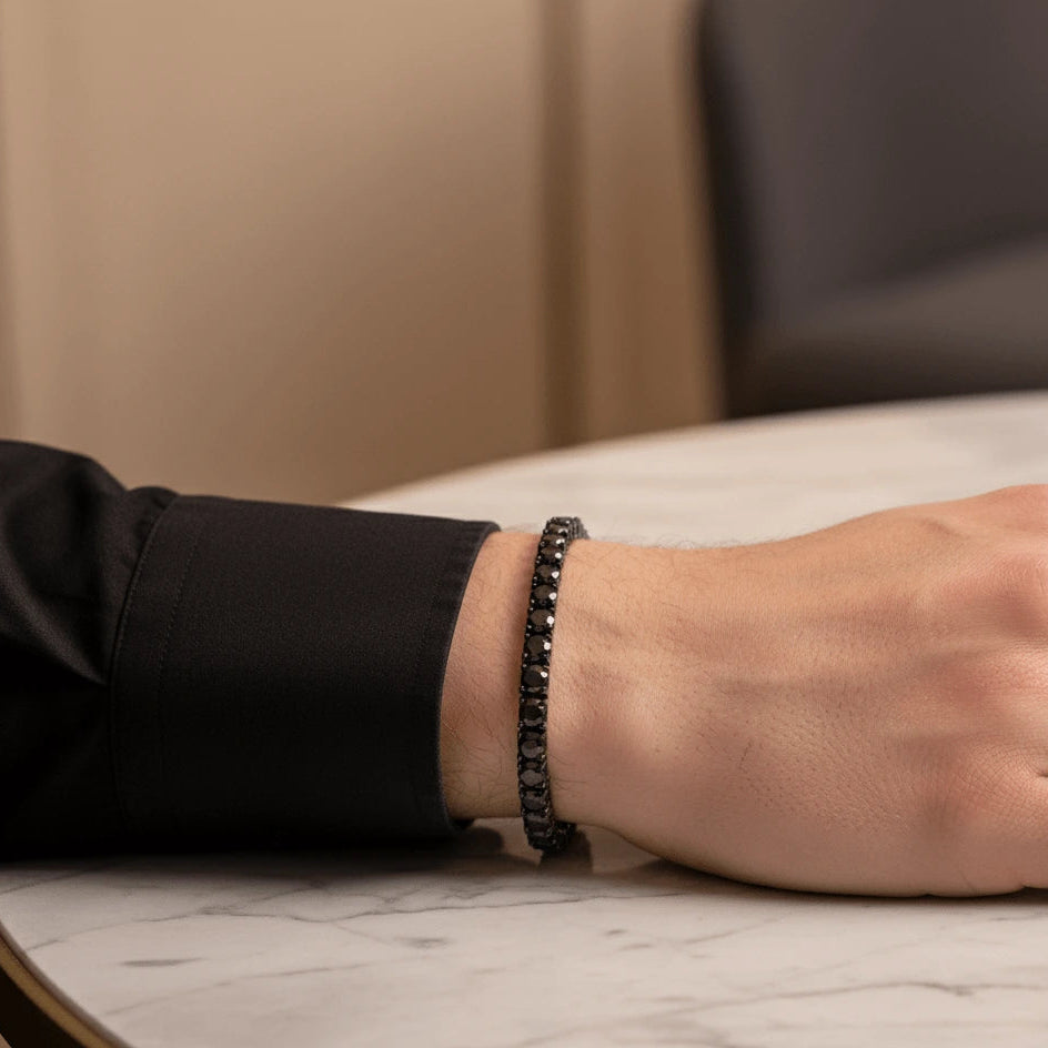 Close-up of man’s wrist wearing 5mm black moissanite tennis bracelet in black gold plating, resting on marble surface – Sensitive Stones