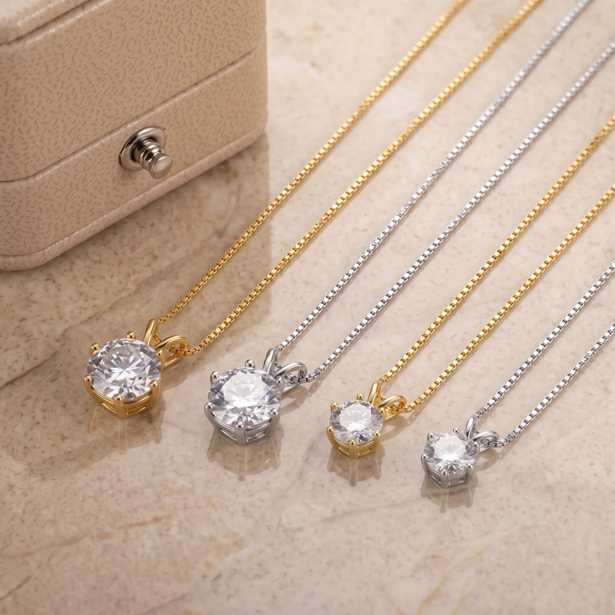 6-prong moissanite solitaire necklaces in white gold and yellow gold finishes shown in two stone sizes on a stone surface beside a jewelry box - Sensitive Stones