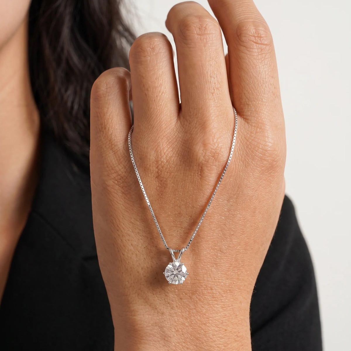 6-prong moissanite solitaire necklace in a white gold finish draped over the back of a hand showing the colorless round brilliant stone - Sensitive Stones