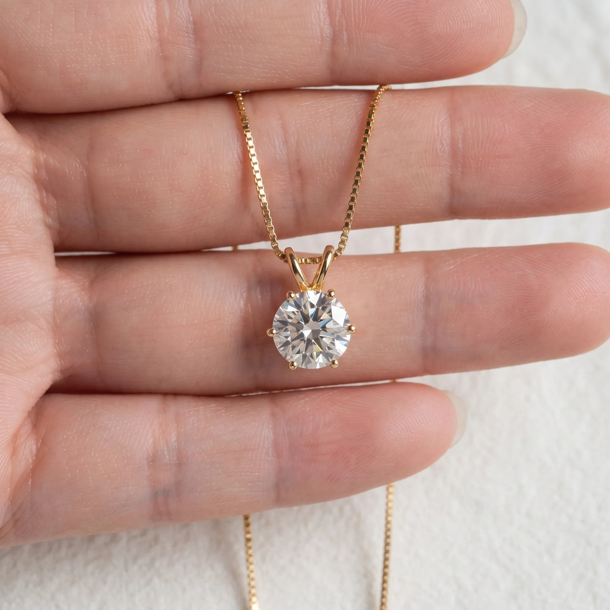 6-prong moissanite solitaire necklace in 925 sterling silver with a yellow gold finish held in the hand to show the pendant size on a box chain - Sensitive Stones