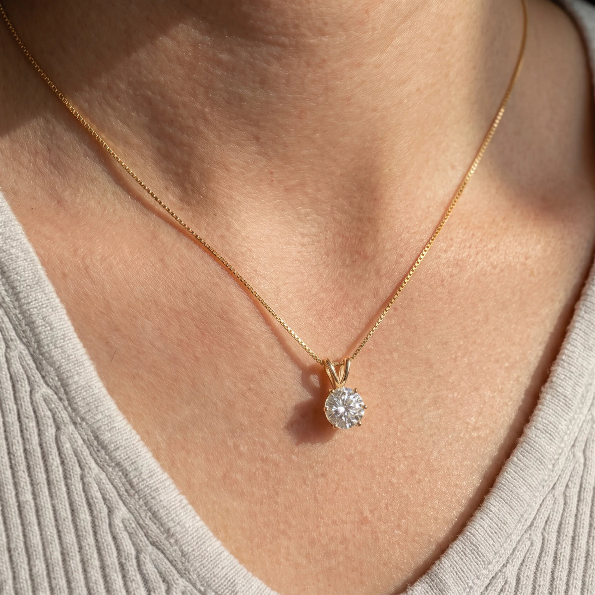 Woman wearing the 6-prong moissanite solitaire necklace in 925 sterling silver with a yellow gold finish at the collarbone - Sensitive Stones