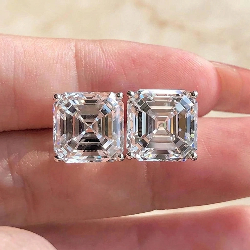 Pair of asscher cut moissanite stud earrings in white gold held on the fingertips, cream background - Sensitive Stones