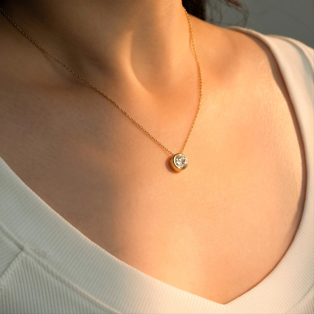 Woman wearing 1ct bezel moissanite pendant necklace in 18K gold plating on delicate O-chain in natural sunlight - Sensitive Stones
