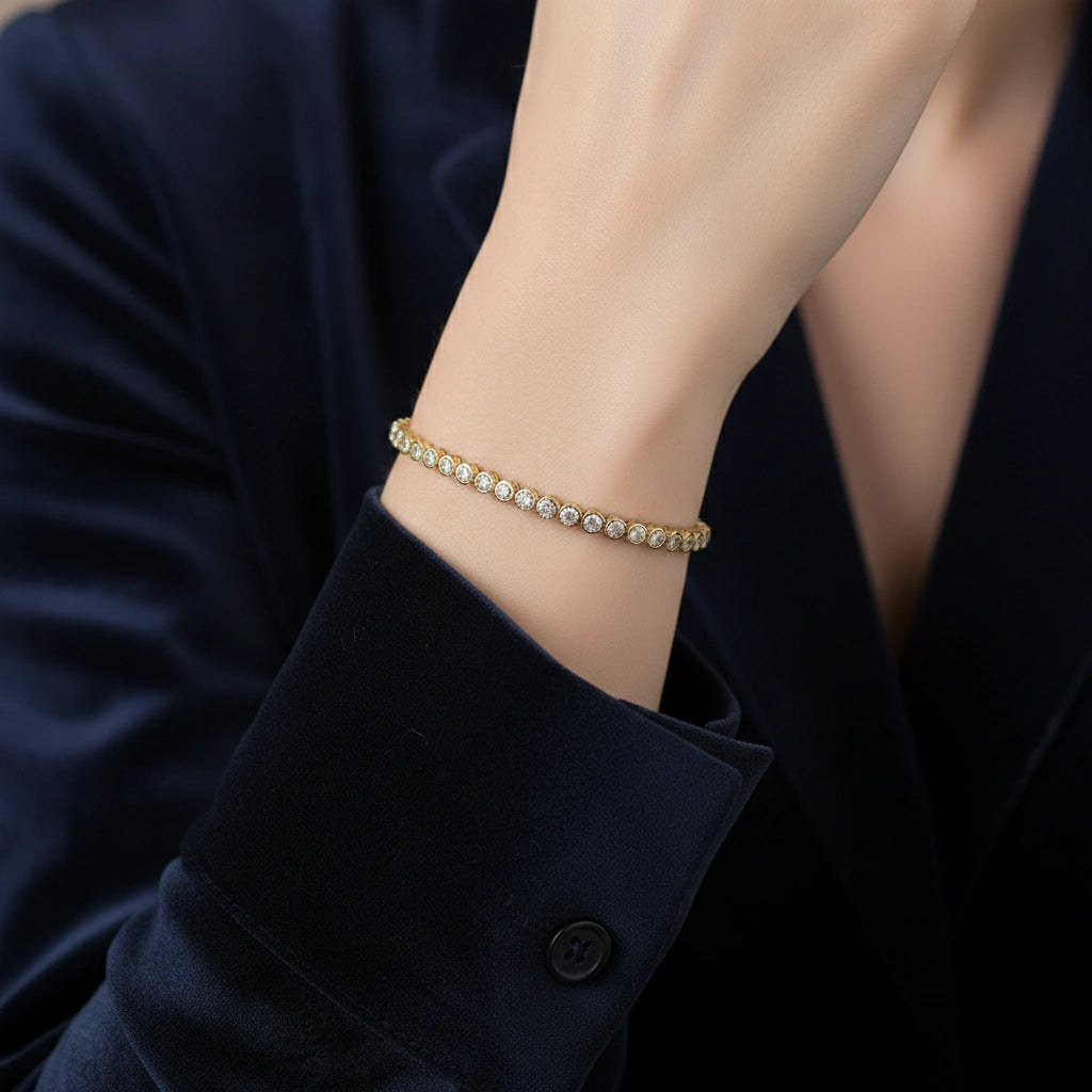 Woman wearing a 2mm bezel moissanite tennis bracelet with D color VVS1 stones in 925 sterling silver and 18k yellow gold finish, styled with dark outfit - Sensitive Stones