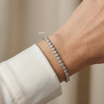 A woman's wrist wearing a 3mm bezel moissanite tennis bracelet in white gold, styled with a soft white outfit - Sensitive Stones
