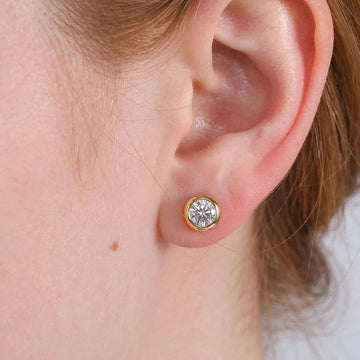 Close up of an ear wearing 0.5ct bezel set moissanite stud earring in 925 sterling silver and 14k gold  showing brilliant cut stone and flush fit - Sensitive Stones