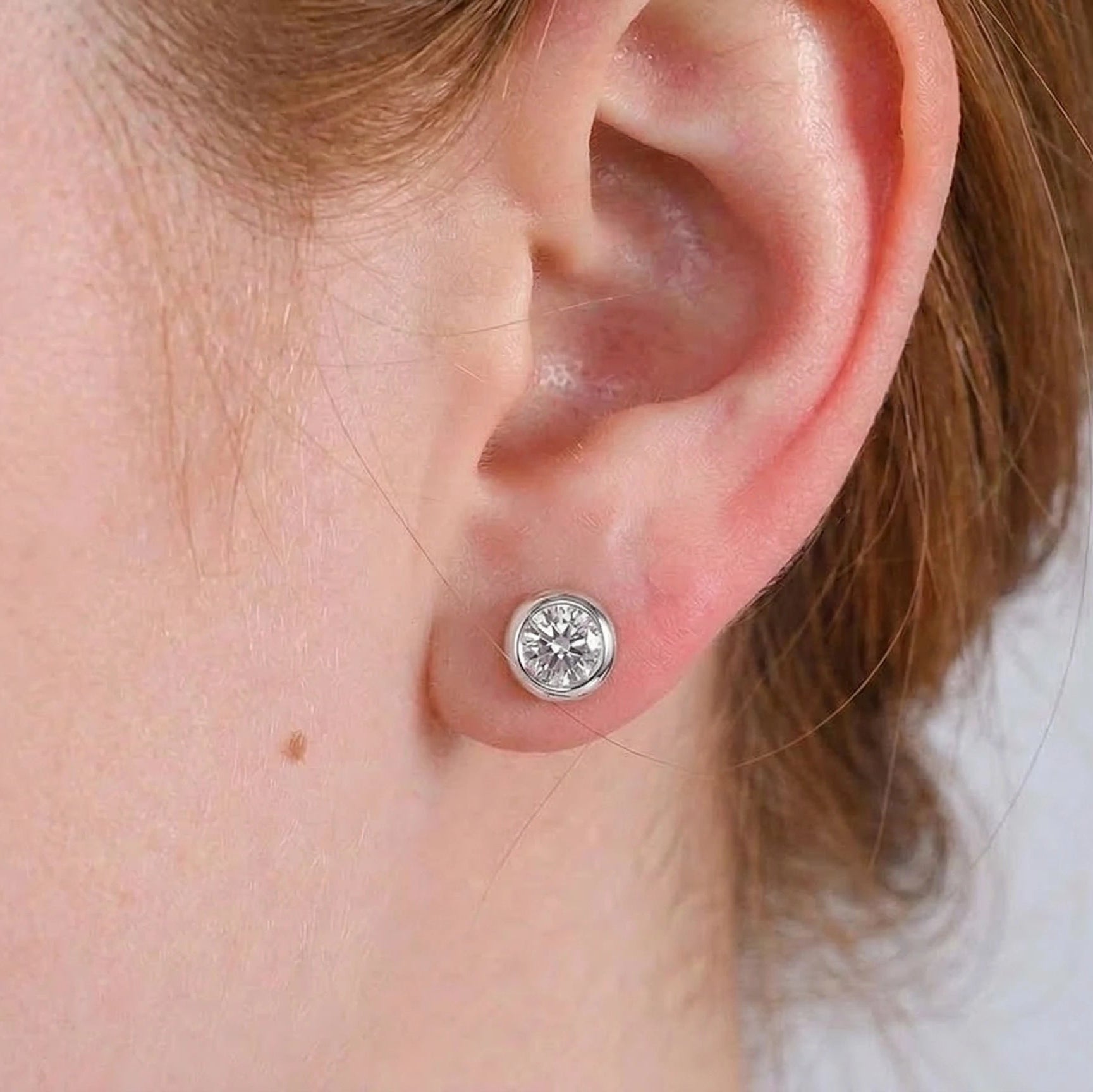 Close up of an ear wearing 0.5ct bezel set moissanite stud earring in 925 sterling silver showing brilliant cut stone and flush fit - Sensitive Stones