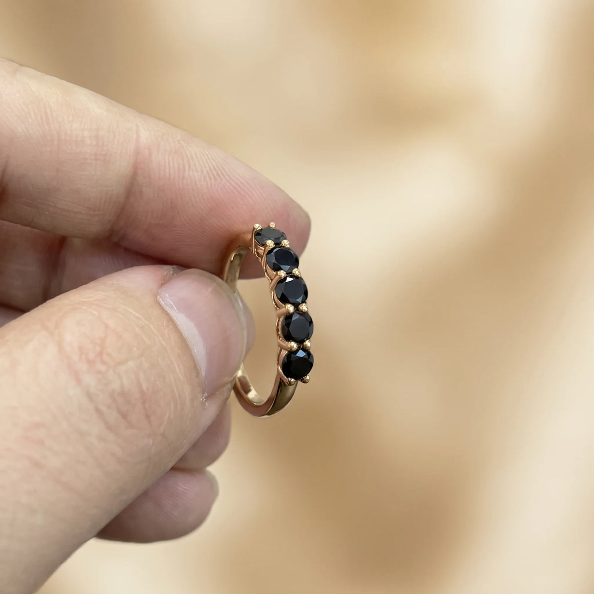 Black moissanite five stone stackable ring in 14K gold filled held between fingers, showing the slim band and mirror-polished black stones - Sensitive Stones