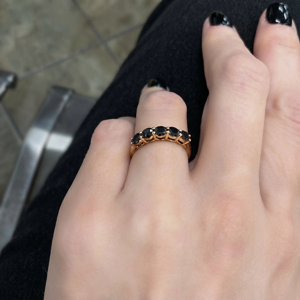 Black moissanite five stone stackable ring in 14K gold filled worn on a hand with a dark manicure, showing the contrast of black stones against gold - Sensitive Stones