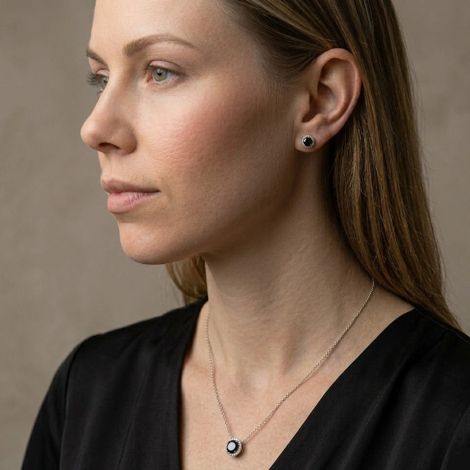 Close-up of of a woman wearing 0.8ct black moissanite halo stud earring on ear and 1ct black moissanite halo pendant necklace in an elegant black dress outfit - Sensitive Stones