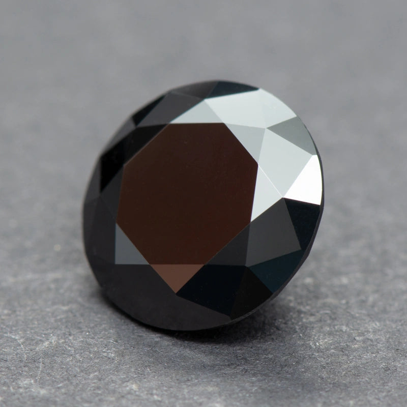 Faceted black moissanite on a gray background - Sensitive Stones
