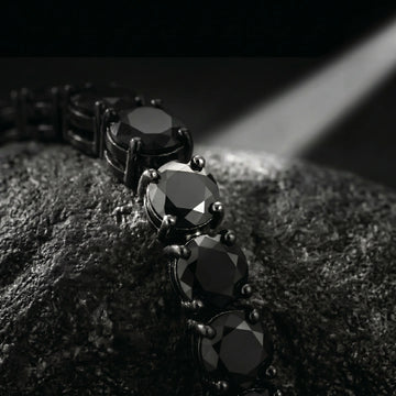 Macro close-up of black moissanite tennis bracelet showing faceted stones and 4-prong setting in dramatic dark lighting - Sensitive Stones