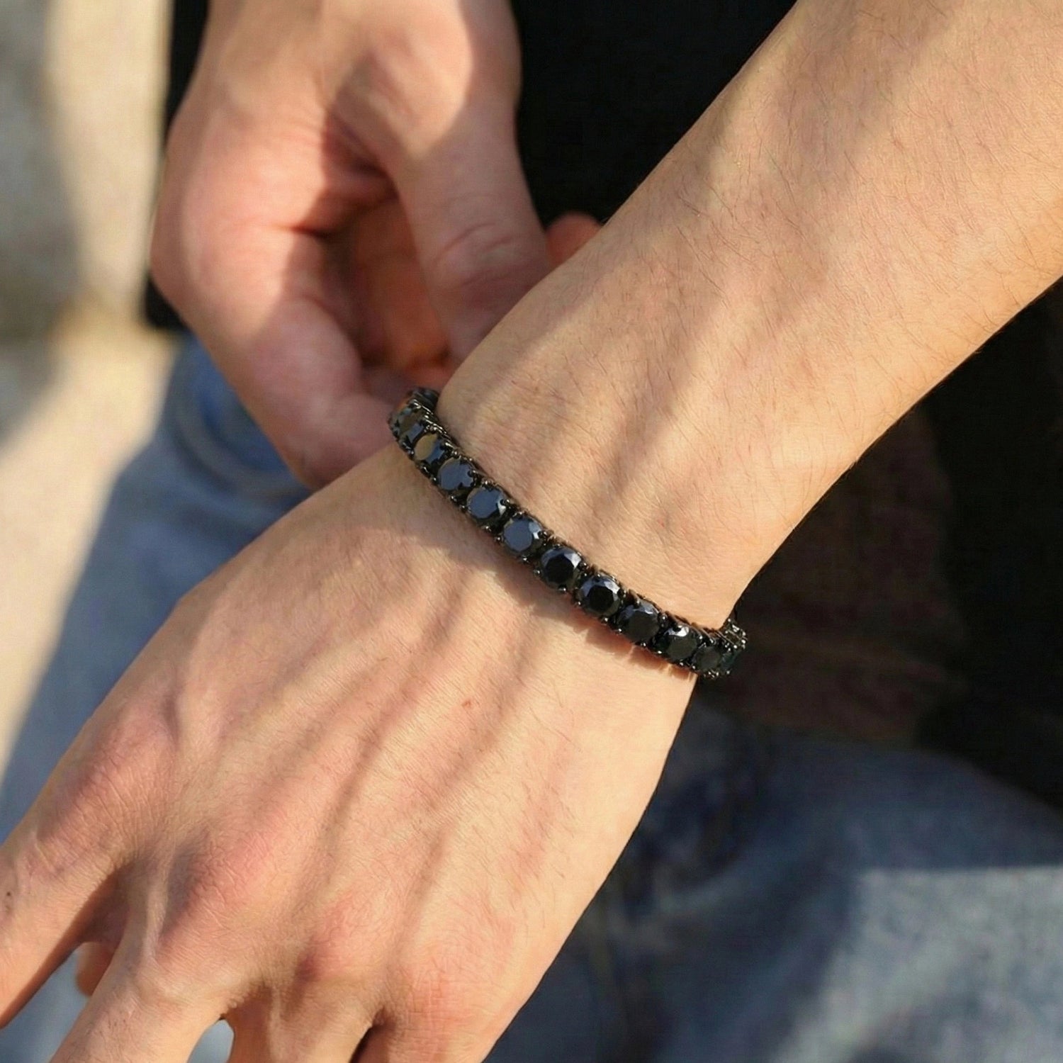 Close-up of a man's wrist wearing a black moissanite tennis bracelet in a simple black t shirt and jeans - Sensitive Stones