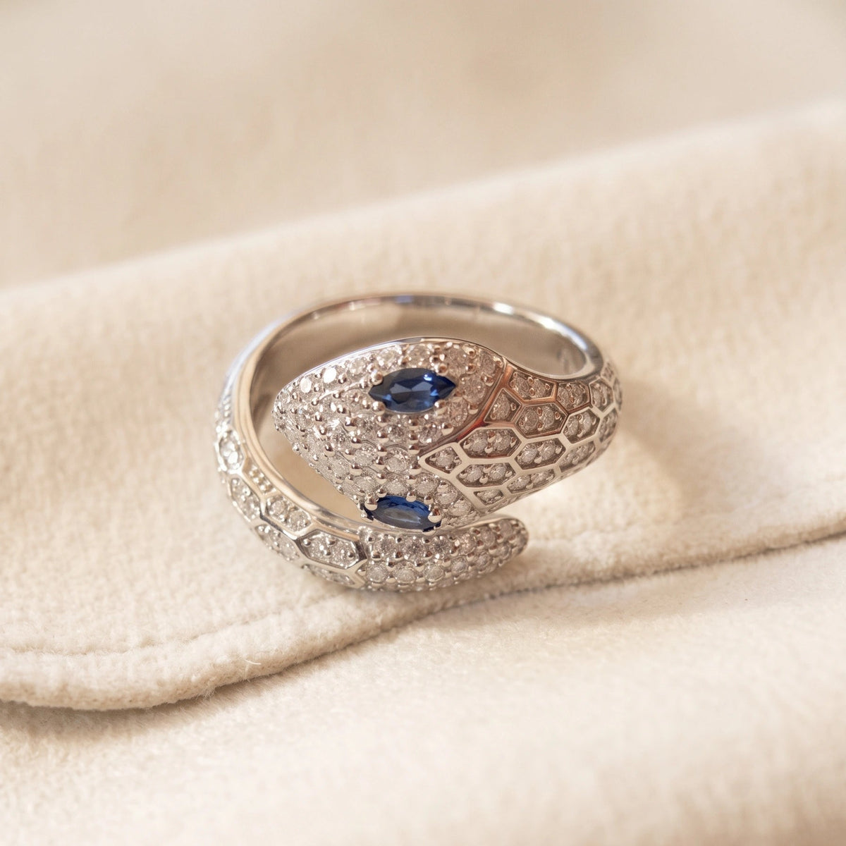 Blue-eyed moissanite snake ring in 925 sterling silver with a white gold finish resting on cream fabric - Sensitive Stones