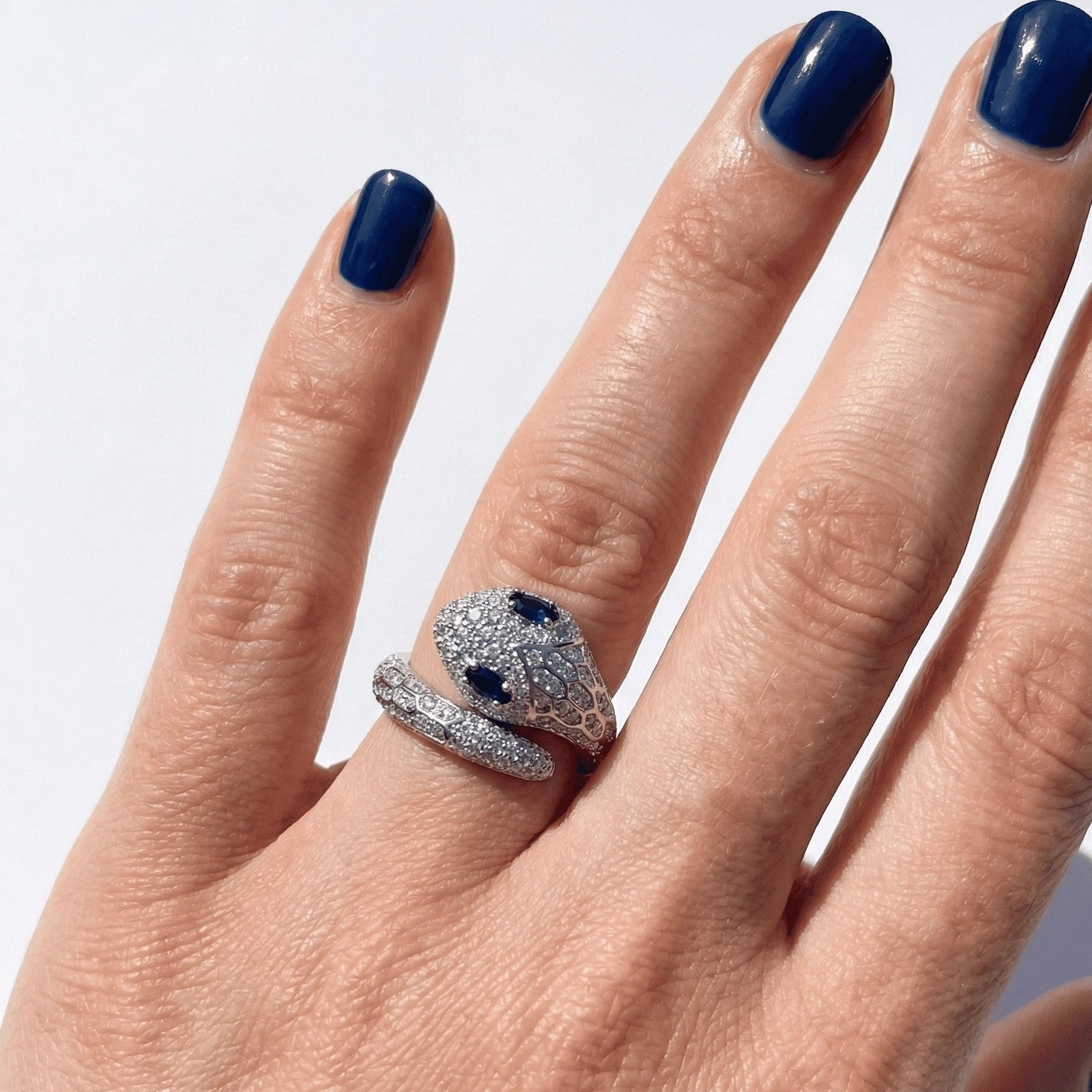 Woman's hand wearing the blue-eyed moissanite snake ring in a white gold finish, showing the pavé serpent and blue stone eyes - Sensitive Stones