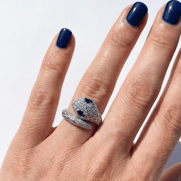 Woman's hand wearing the blue-eyed moissanite snake ring in a white gold finish, showing the pavé serpent and blue stone eyes - Sensitive Stones