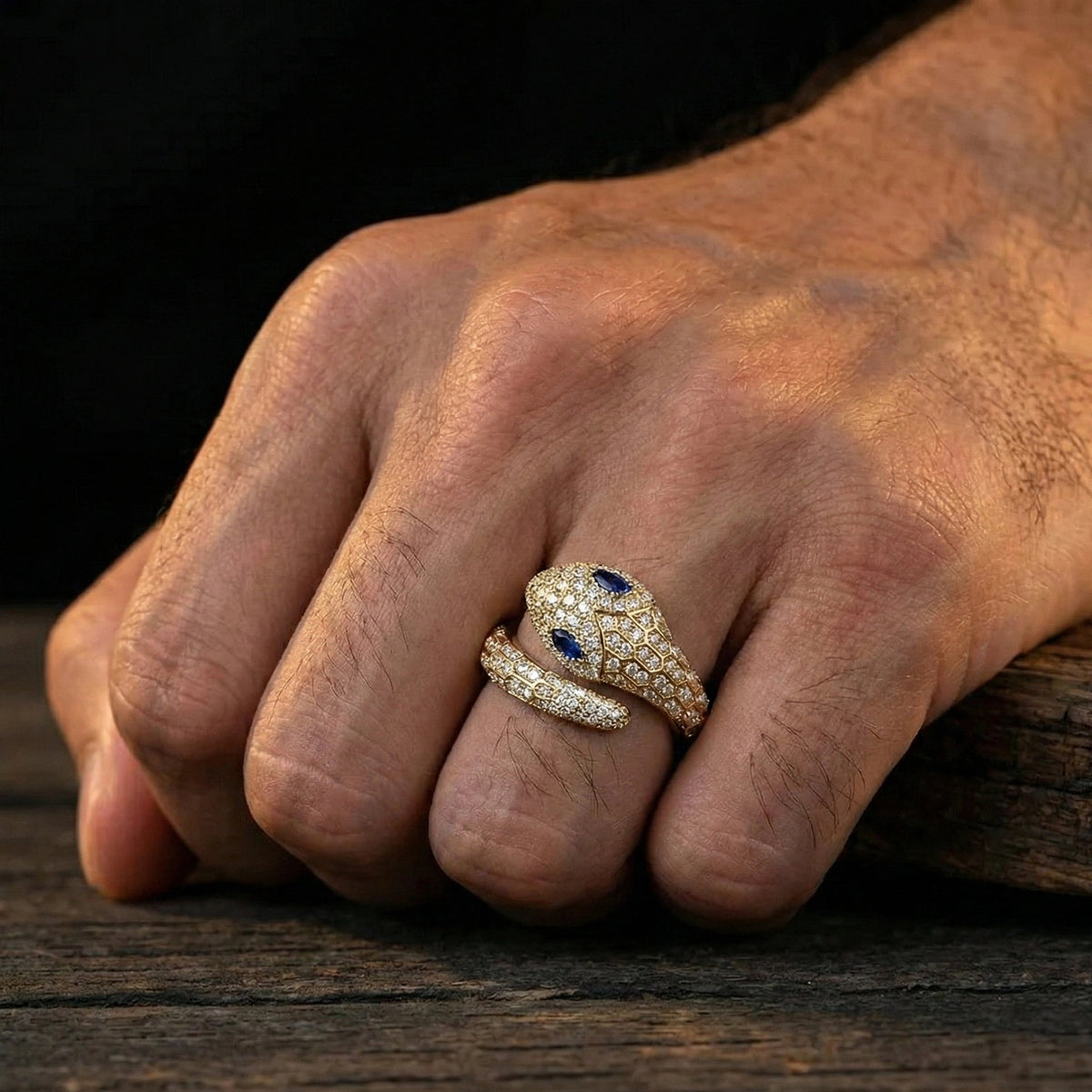 Man's hand wearing the blue-eyed moissanite snake ring in a yellow gold finish with pavé moissanite and blue lab-created stone eyes - Sensitive Stones