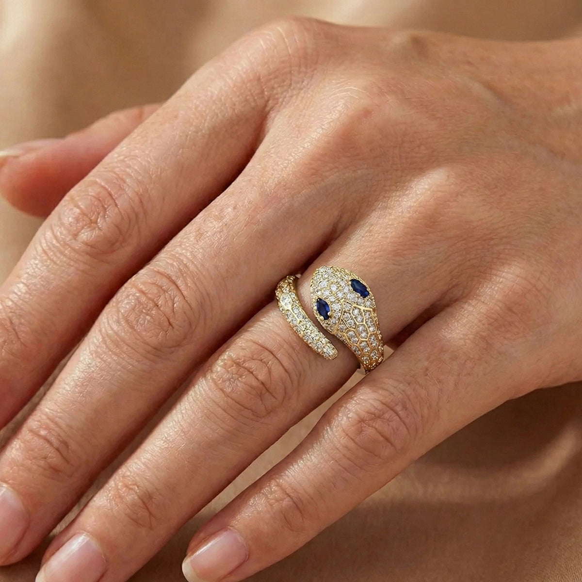 Woman's hand wearing the blue-eyed moissanite snake ring in a yellow gold finish with pavé moissanite and blue stone eyes - Sensitive Stones