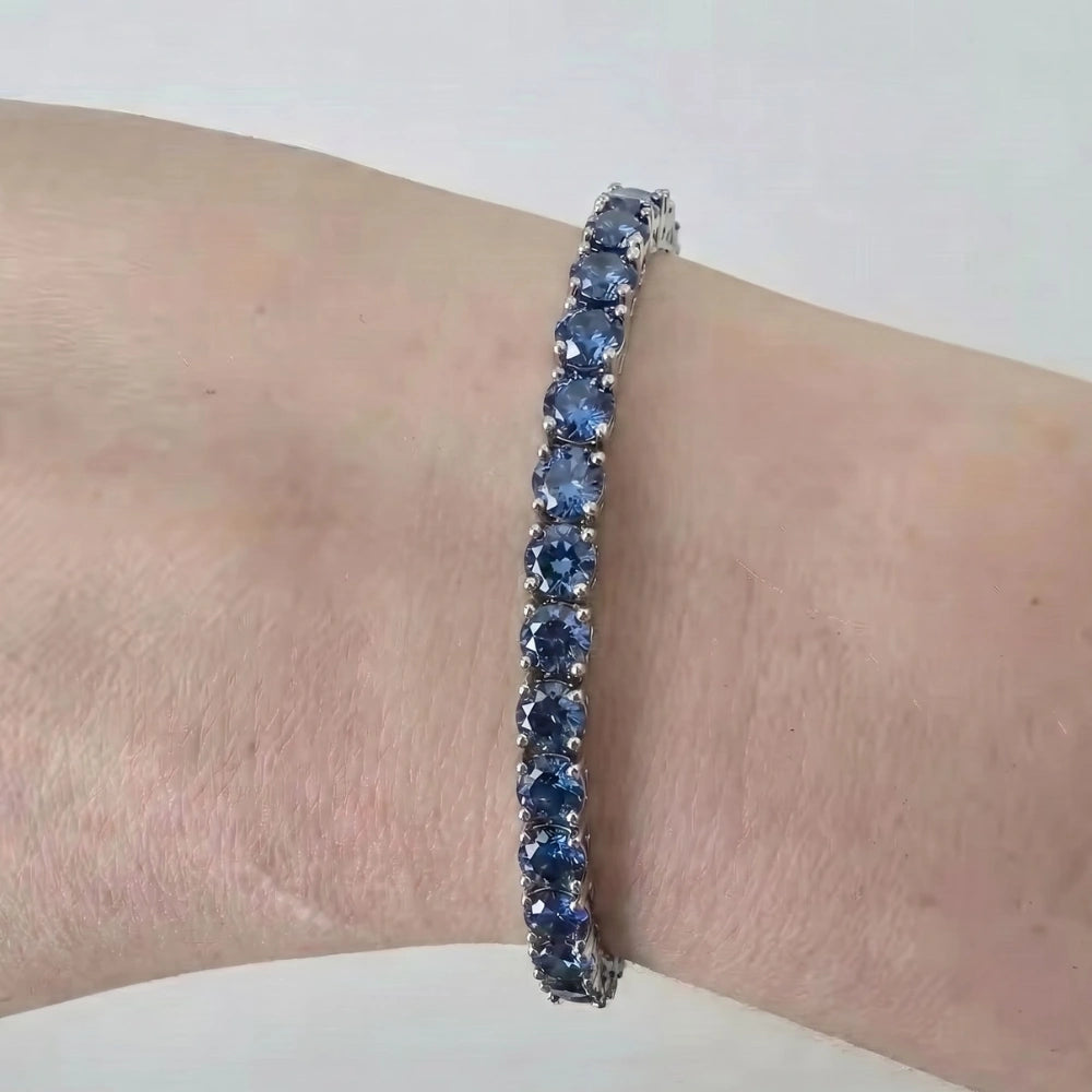A close-up of blue moissanite tennis bracelet worn on a person's wrist against a plain light background - Sensitive Stones