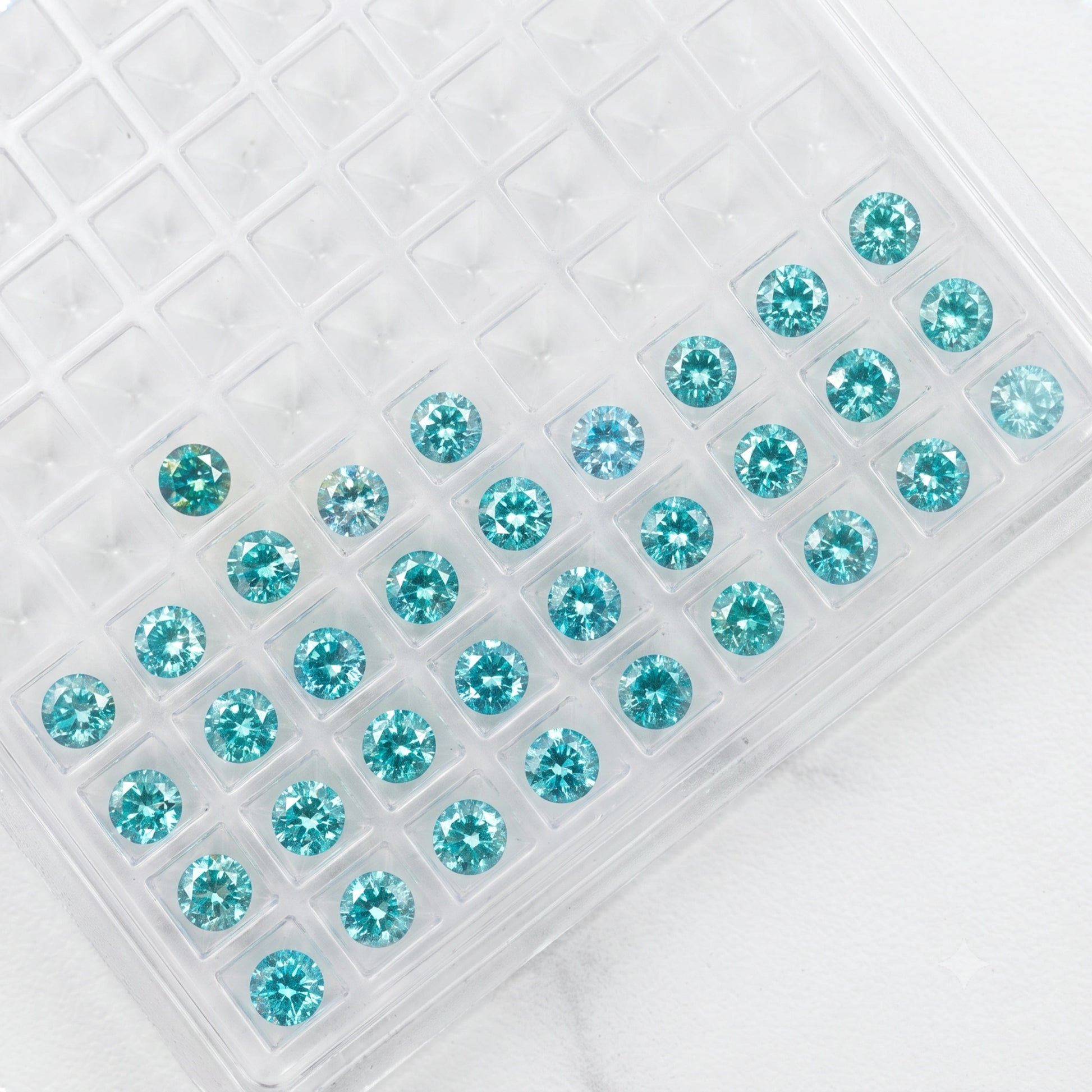 Brilliant-cut loose blue moissanite stones arranged in a clear display tray against a clean white background - Sensitive Stones