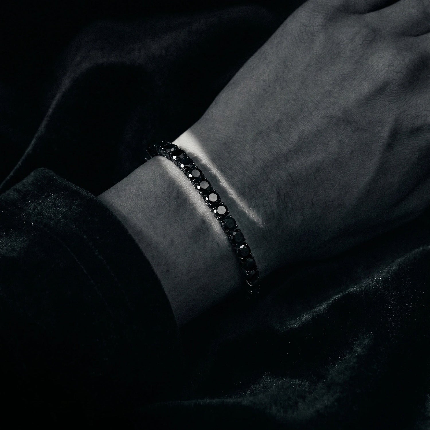 Close-up of a wrist wearing black moissanite tennis bracelet with a dark background - Sensitive Stones