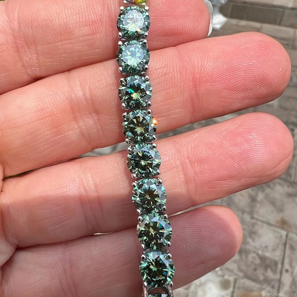 Close-up of a hand holding a green moissanite tennis bracelet set in 925 sterling silver under natural sunlight - Sensitive Stones