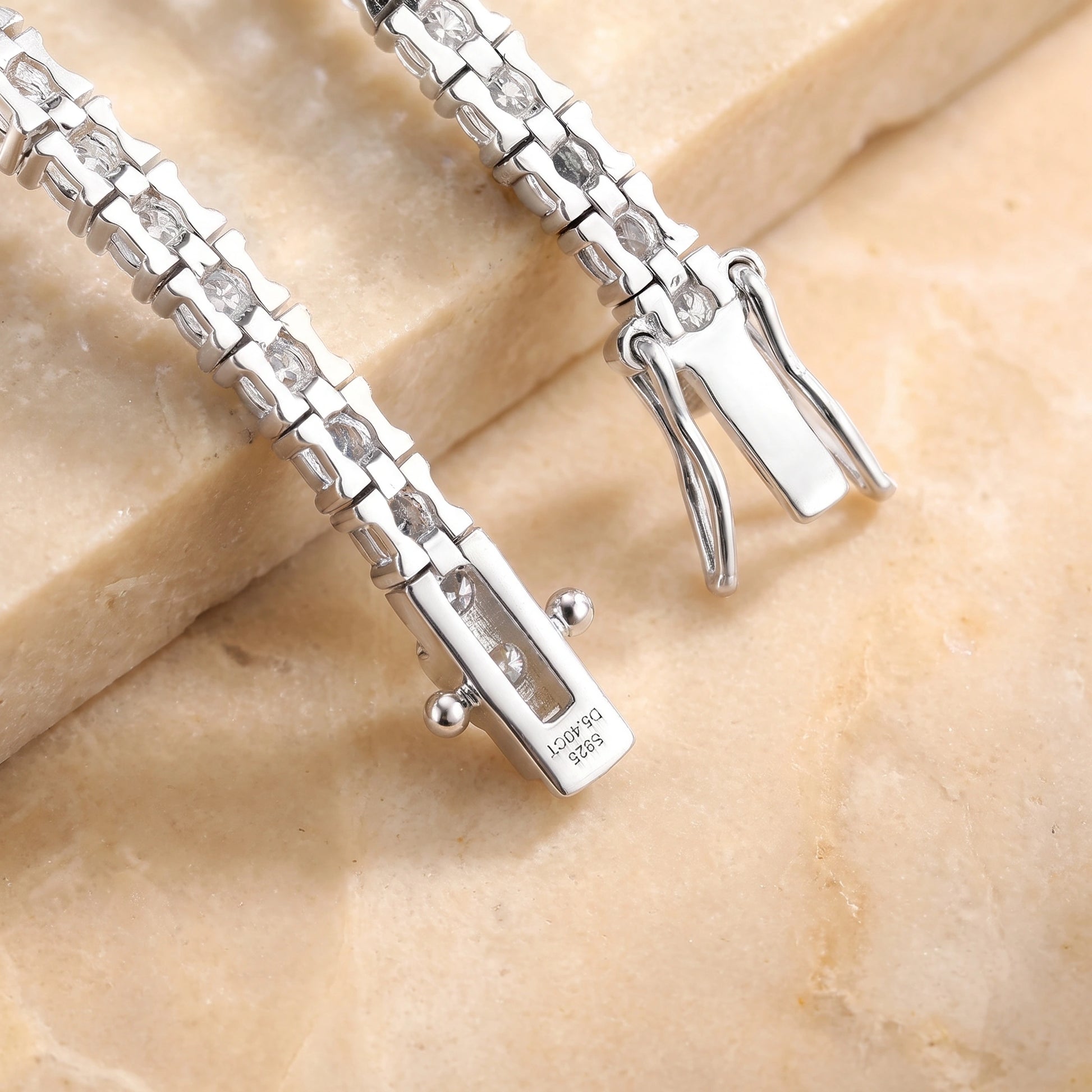 Close-up of a white gold moissanite tennis bracelet box clasp with a stamped S925 mark, resting on a beige stone slab - Sensitive Stones