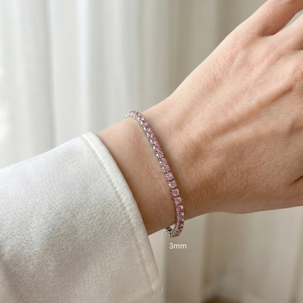 Close up of a wrist wearing 3mm pink moissanite tennis bracelet with round-cut stones in white gold plated sterling silver, worn with white outfit - Sensitive Stones