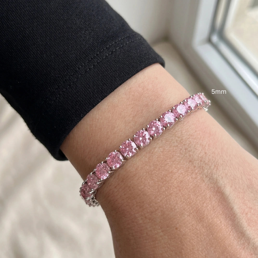 Close up of a wrist wearing 5mm pink moissanite tennis bracelet with round-cut stones in white gold plated sterling silver, worn with black outfit - Sensitive Stones