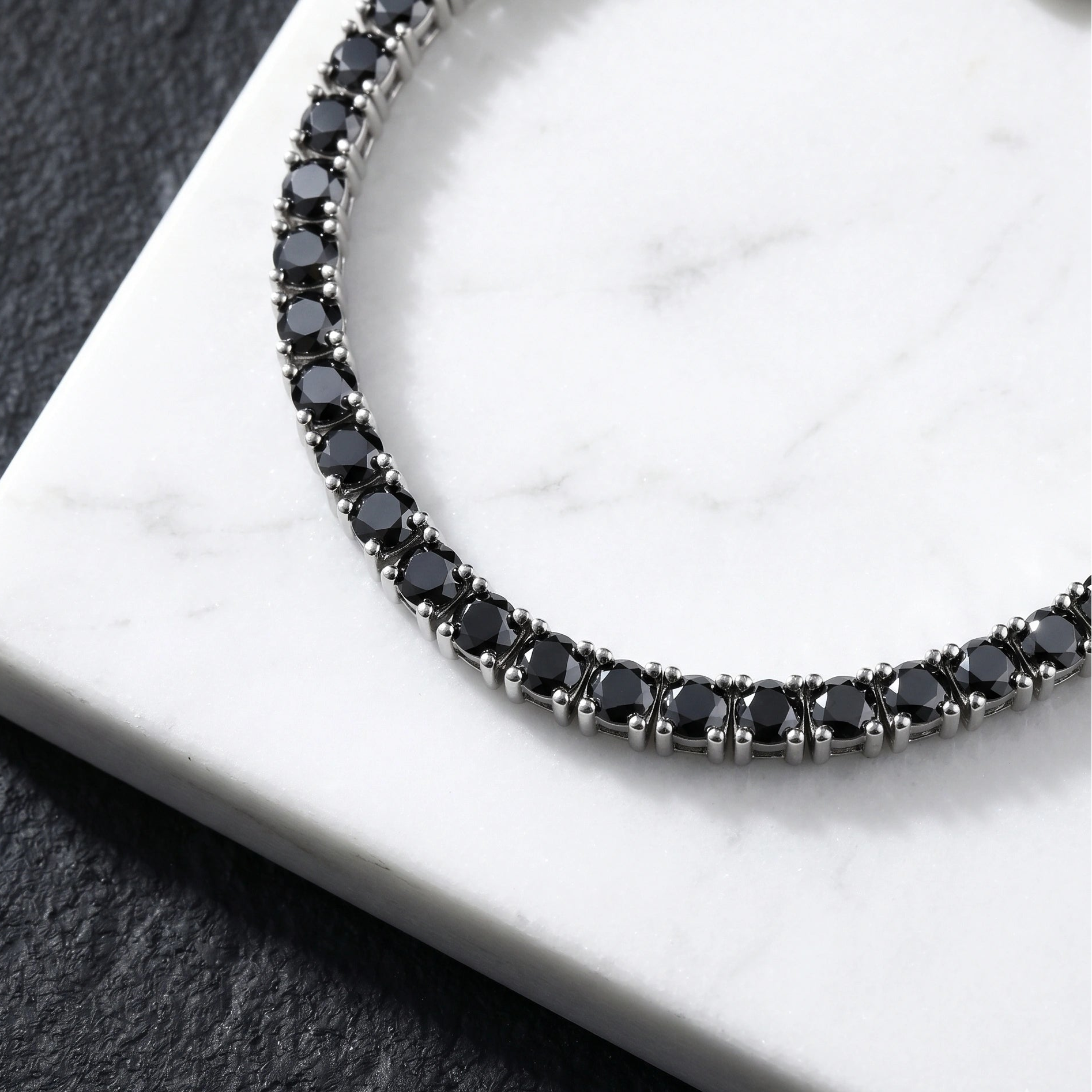 Close up of black moissanite tennis bracelet in 925 sterling silver with white gold plating on a white marble surface - Sensitive Stones